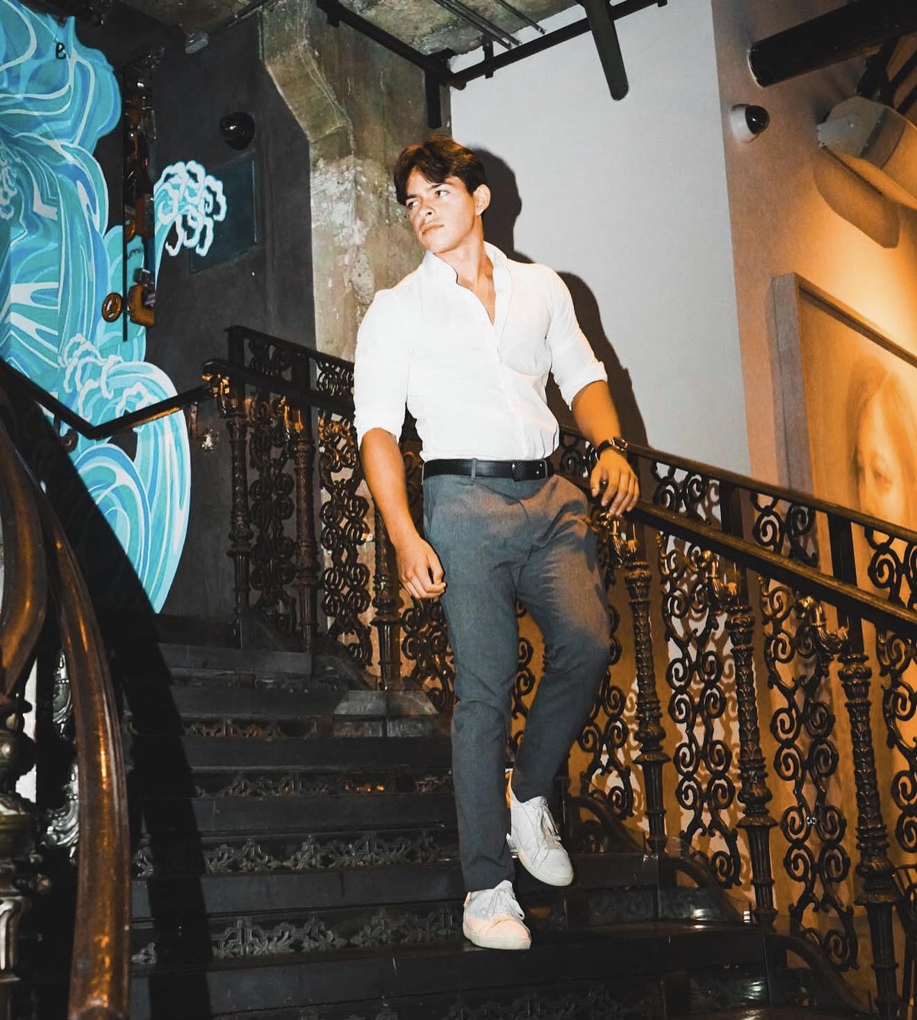 Portrait on a staircase, wearing a white shirt and gray trousers.